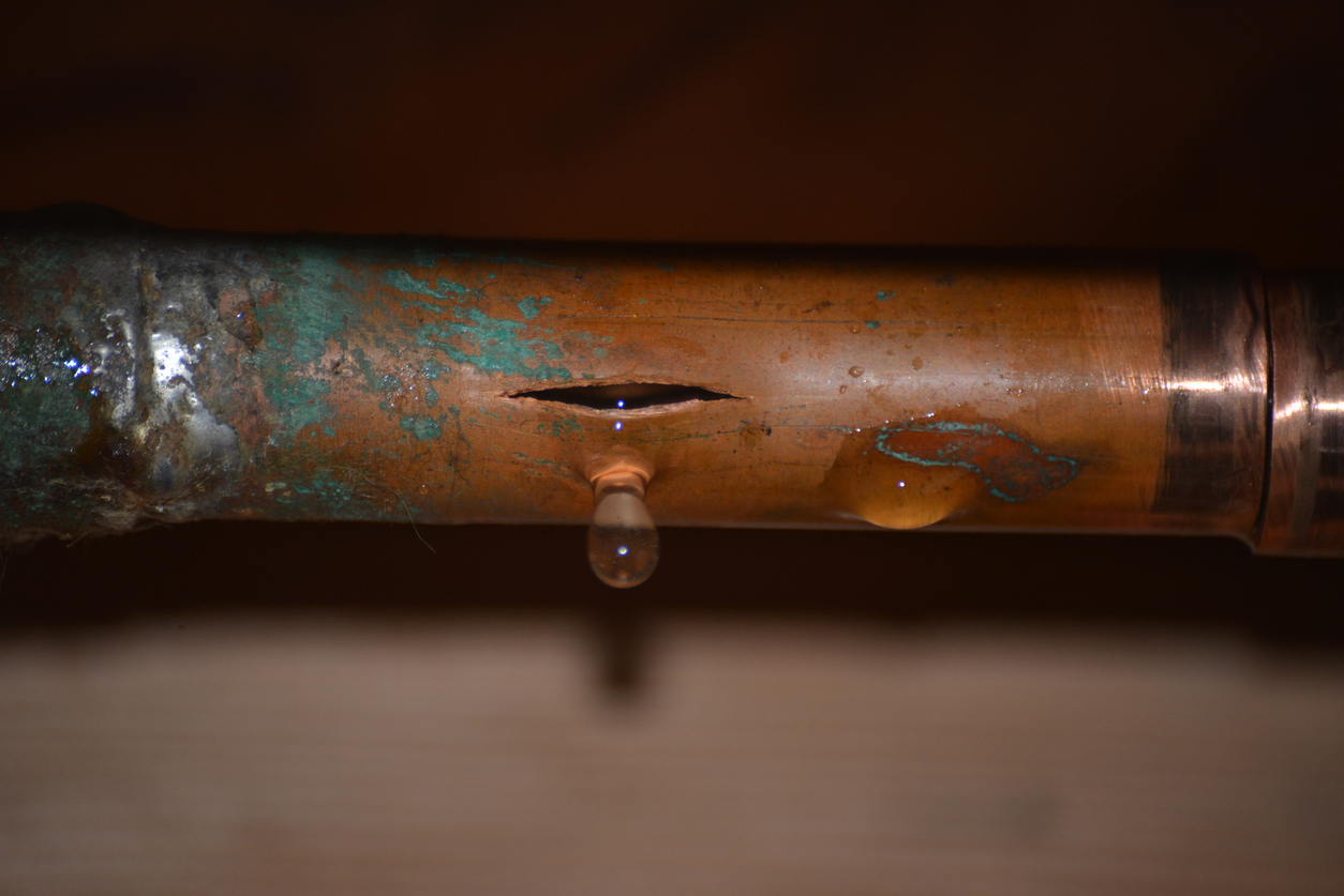 A ruptured copper pipe with ice on it and water dripping from a crack caused by the pipe freezing.