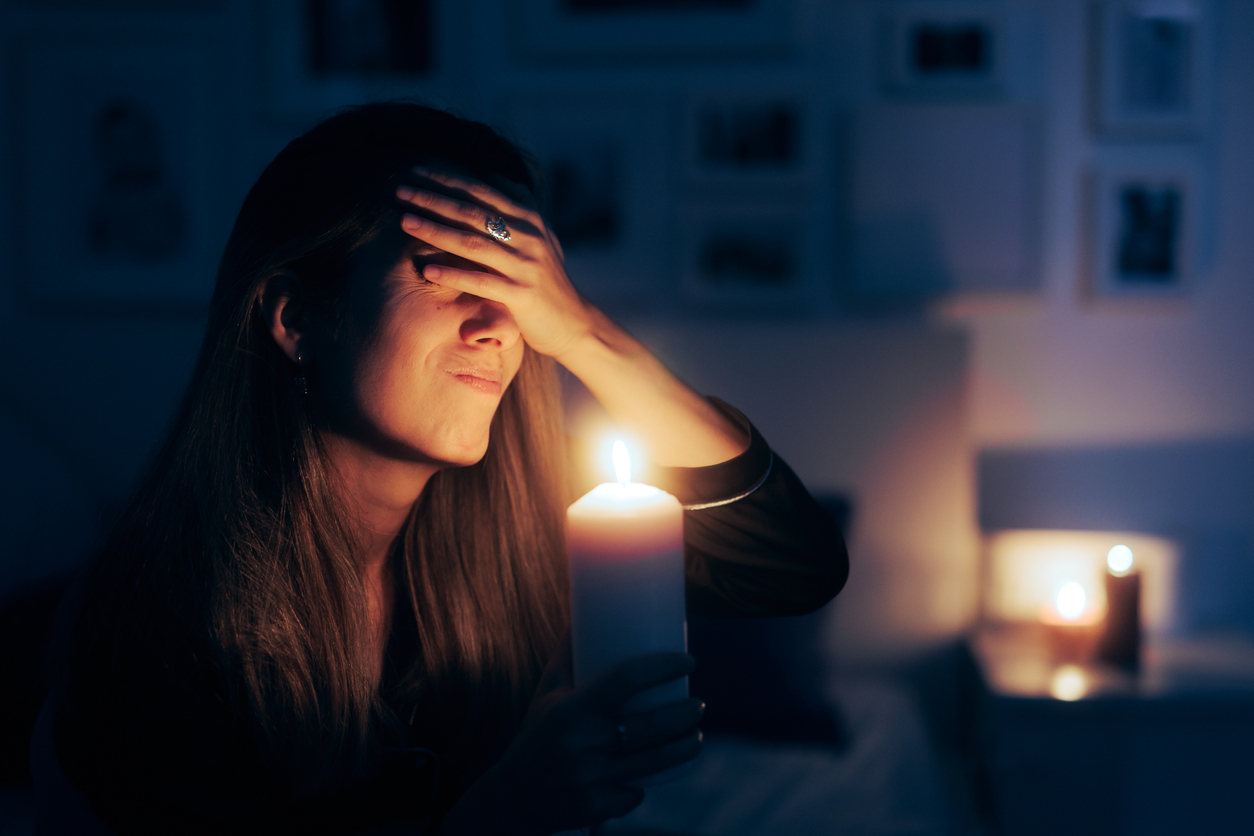 Woman holding up candle while struggling with the effects of a power outage in her home.